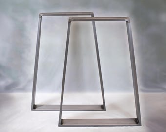 Può includere: Due gambe per tavolo in metallo con finitura grigia. Le gambe hanno una forma a A con un piano superiore piatto.