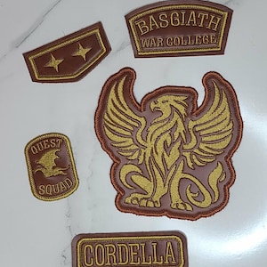 May include: A collection of five brown and gold embroidered patches. One patch features a griffin, another reads BASGIATH WAR COLLEGE, one says QUEST SQUAD with a dragon icon, one displays two stars, and the final rectangular patch reads CORDELLA.