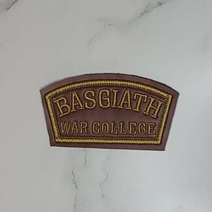 May include: A brown, arched, faux leather patch featuring gold embroidered text that reads BASGIATH WAR COLLEGE. The patch has a gold stitched border and a smooth, matte finish, designed for application onto fabric or other surfaces.