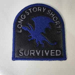 Puede incluir: Un parche bordado semicircular con fondo negro y borde azul. Presenta la silueta azul de un dragón en el centro. El texto "LONG STORY SHORT" está arqueado sobre el dragón y la palabra "SURVIVED" aparece en color gris en la parte inferior.