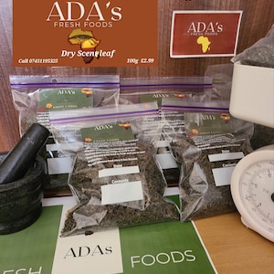 May include: Multiple clear plastic bags filled with dried scent leaf, branded "ADA's FRESH FOODS." The bags are displayed on a wooden surface, with a mortar and pestle to the left. Text on the image reads "Dried scent leaf 100g".