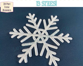 May include: White embroidered snowflake design. The image includes the text "LewisEmbroideryCo", "13 SIZES!", and "3D PUFF FOAM REQUIRED". The snowflake is centered on a dark blue background.