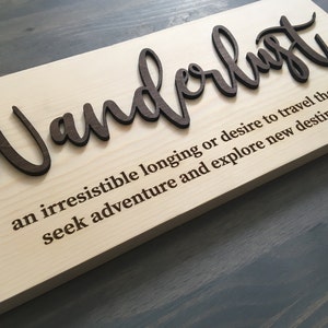 May include: A wooden sign with the word "Wanderlust" in raised letters. The definition of wanderlust is written below: "an irresistible longing or desire to travel the world, seek adventure and explore new destinations."