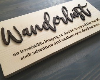 May include: A wooden sign with the word "Wanderlust" in raised letters. The definition of wanderlust is written below: "an irresistible longing or desire to travel the world, seek adventure and explore new destinations."