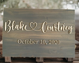 May include: A rustic wooden sign with the names "Blake & Courtney" and the date "October 10, 2020" in a cursive font.