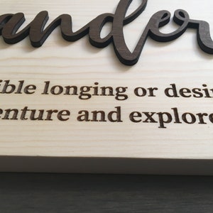 May include: Wooden sign with the word "wanderlust" in brown lettering. The definition of wanderlust is "an irresistible longing or desire to travel and explore new places."