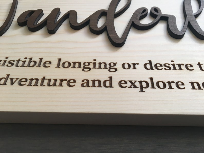 May include: Wooden sign with the word "wanderlust" in brown lettering. The definition of wanderlust is "an irresistible longing or desire to travel and explore new places."