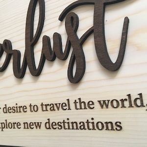 May include: A wooden sign with the word "wanderlust" written in a decorative font. The sign also includes the definition of wanderlust: "a strong longing or desire to travel the world, and explore new destinations."