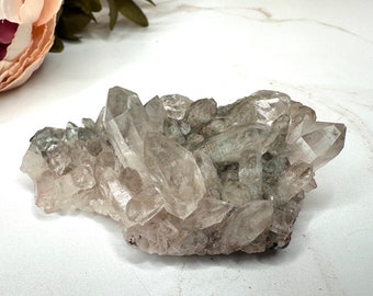 May include: A cluster of clear quartz crystals with a gray, cloudy appearance. The crystals are arranged in a natural, organic formation.