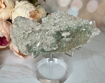 May include: A green and white crystal cluster on a clear acrylic stand. The crystal has a rough, natural texture and is composed of many small crystals.