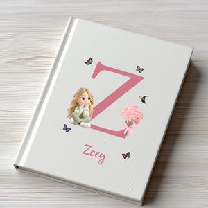 May include: A personalized journal with a white cover featuring a large pink letter "Z" and the name "Zoey". Adorning the cover are butterfly illustrations, a bouquet of pink flowers, and a figurine of a girl.
