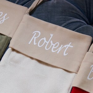 May include: A beige stocking with a white fabric cuff that says "Robert" in a cursive font.