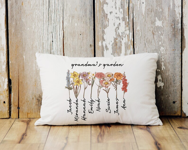 May include: White rectangular pillow with the text "grandma's garden" and names of family members. The pillow features a floral design with various flowers in shades of yellow, purple, pink, and orange.