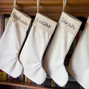 May include: Three white Christmas stockings with the names "Joshua", "Lucas", and "Sarah" embroidered on them.