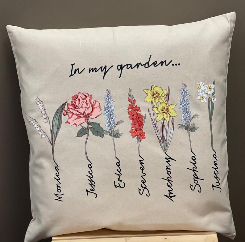 May include: Beige square pillow with the text "In my garden..." and floral illustrations. The flowers include a rose, daffodils, and other blooms, each with a name below. The names are Monica, Jessica, Erica, Steven, Anthony, Sophia, and Justina.