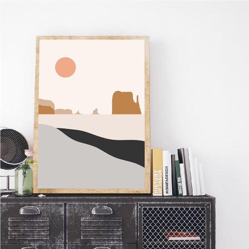 Puede incluir: Impresi&oacute;n de arte abstracto con un dise&ntilde;o minimalista que presenta un sol de color melocot&oacute;n, monta&ntilde;as marrones y un paisaje gris y negro. La impresi&oacute;n est&aacute; enmarcada en un marco de madera claro.