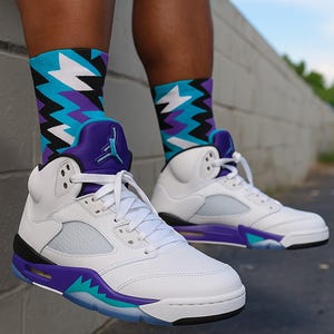 May include: White and purple Air Jordan 5 sneakers with teal and purple accents. The sneakers are paired with patterned socks in teal, purple, black, and white. The text "FRESH OFF THE VINE" is at the bottom of the image.