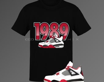 Peut inclure: T-shirt noir avec un imprimé de chaussure de basket-ball rouge et blanche et le texte "1989". Une chaussure de basket-ball rouge et blanche est également représentée.