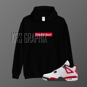Op de afbeelding: Zwarte hoodie met de tekst "Sneakerhead" in een rode box op de voorkant. Witte en rode sneakers met zwarte accenten.