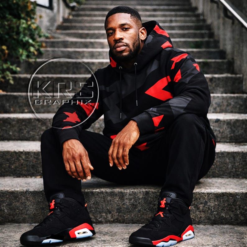 Pu&ograve; includere: Una persona indossa una felpa con cappuccio nera e rossa a fantasia e pantaloni abbinati, seduta su gradini di cemento. La felpa con cappuccio e i pantaloni presentano un design geometrico con dettagli rossi. Le scarpe da ginnastica nere con dettagli rossi e bianchi completano l'outfit. Il testo "KRS Graphix" &egrave; incluso.