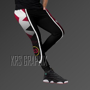 May include: Black sweatpants with a white and red geometric design. The sweatpants have a white stripe down the side and a yellow circle with the number 23 on the left leg.