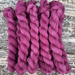 May include: A bundle of six skeins of deep pink yarn. The yarn is a soft, fuzzy texture and is perfect for knitting or crocheting.