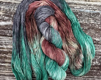 Puede incluir: Un ovillo de hilo en tonos de verde, gris y marrón. El hilo está retorcido y doblado, mostrando las transiciones de color.