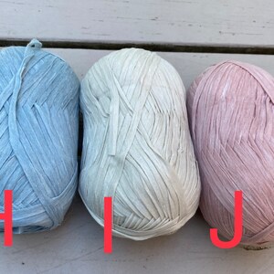 Puede incluir: Tres ovillos de hilo en diferentes colores: azul claro, blanco roto y rosa claro. El hilo est&aacute; hecho de tiras finas y planas de tela.