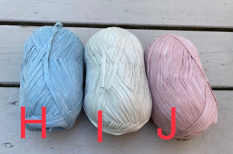 Puede incluir: Tres ovillos de hilo en diferentes colores: azul claro, blanco roto y rosa claro. El hilo est&aacute; hecho de tiras finas y planas de tela.