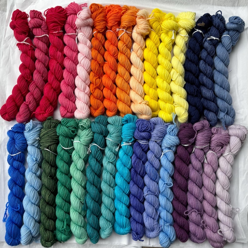 Pu&ograve; includere: Una collezione di 24 gomitoli di filato in vari colori, tra cui rosso, rosa, arancione, giallo, blu, verde e viola. Il filato &egrave; disposto in file, con ogni fila che contiene un colore diverso.