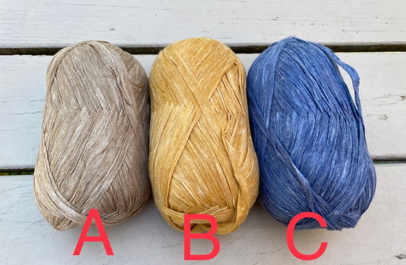 Puede incluir: Tres ovillos de hilo en diferentes colores: beige, amarillo y azul. El hilo es texturizado y tiene un aspecto r&uacute;stico.
