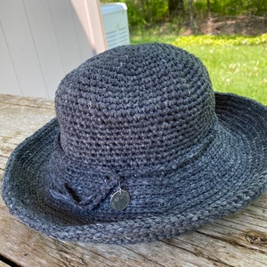 A charcoal gray crocheted sun hat with a wide brim and a small silver charm attached to the front.