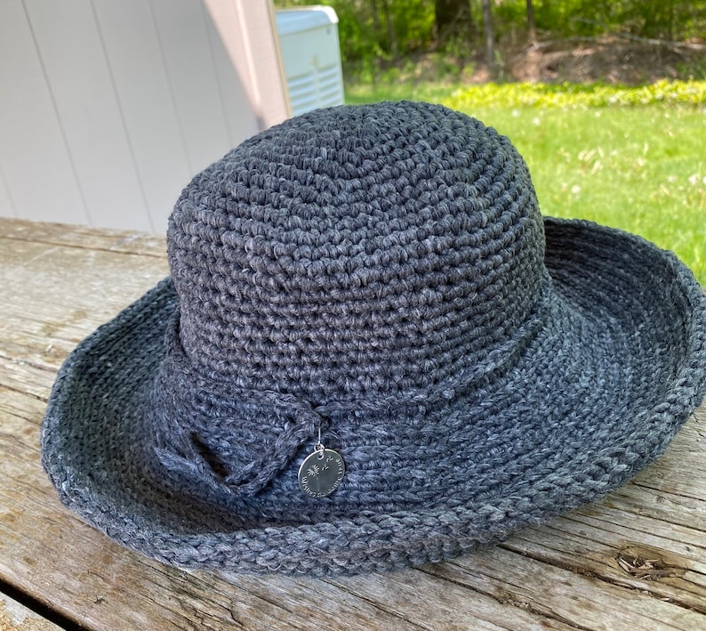A charcoal gray crocheted sun hat with a wide brim and a small silver charm attached to the front.