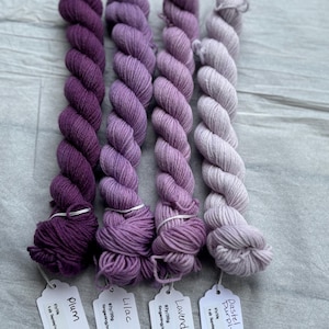 Pu&ograve; includere: Quattro gomitoli di filato fingering tinto a mano in tonalit&agrave; di viola, lilla, lavanda e viola pastello. Ogni gomitolo &egrave; etichettato con il peso del filato, il metraggio e il nome del colore.