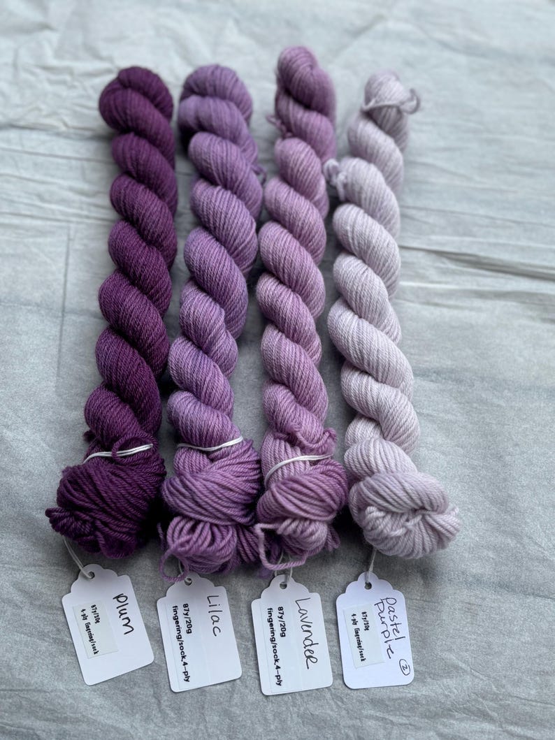 Pu&ograve; includere: Quattro gomitoli di filato fingering tinto a mano in tonalit&agrave; di viola, lilla, lavanda e viola pastello. Ogni gomitolo &egrave; etichettato con il peso del filato, il metraggio e il nome del colore.