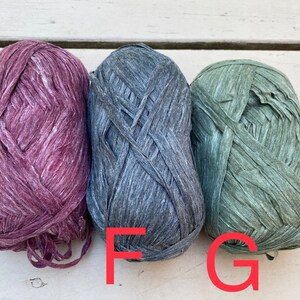 Puede incluir: Tres ovillos de hilo en diferentes colores: morado oscuro, gris oscuro y verde apagado. El hilo est&aacute; hecho de un material texturizado y arrugado.