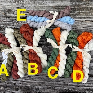 May include: A collection of colorful yarn skeins, each tied with a cream-colored ribbon. The yarn colors include shades of green, orange, brown, and blue. The skeins are arranged on a weathered wooden surface.