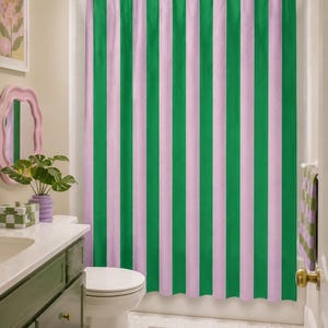 Pode incluir: Uma cortina de duche com riscas verticais em tons alternados de verde vibrante e rosa pastel suave. A cortina está suspensa numa barra branca com argolas brancas, cobrindo o comprimento da área da banheira numa casa de banho.