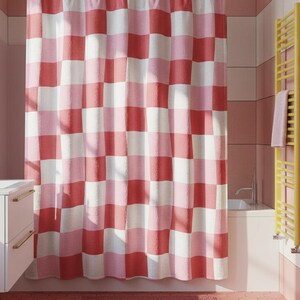 May include: A pink, red, and white checkered shower curtain hangs in a bathroom. The curtain is the focal point, with a repeating pattern of large squares. The bathroom has pink and white tile walls, a white vanity, and a yellow towel rack.