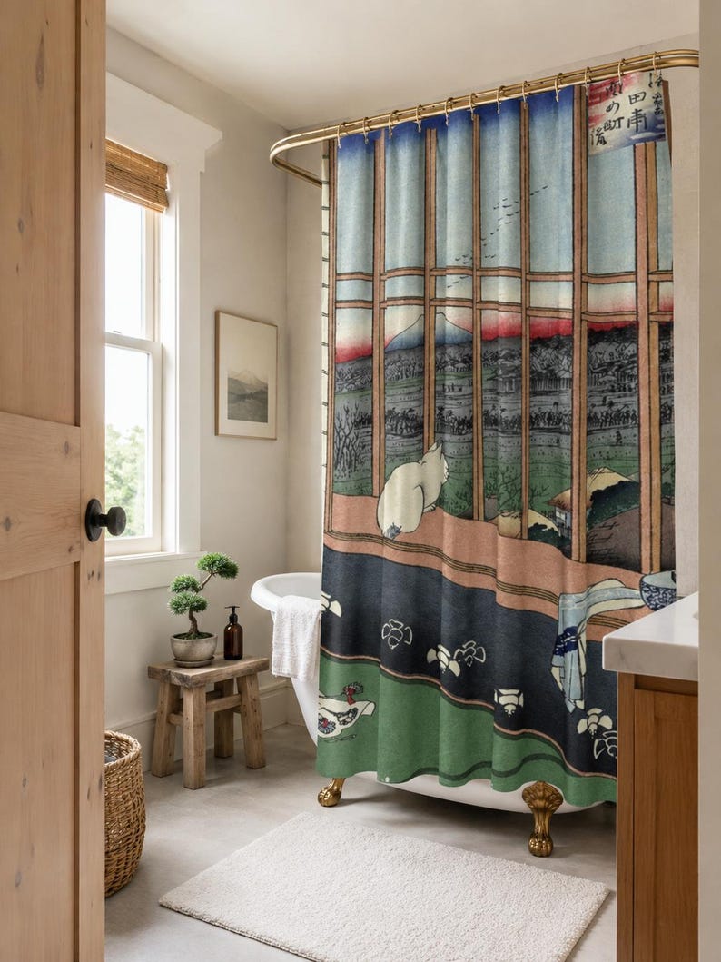 May include: A shower curtain featuring a Japanese woodblock print style illustration of a white cat looking out a window at a landscape with a mountain, blue sky, and green fields. The curtain has a gold-toned rod and rings at the top.