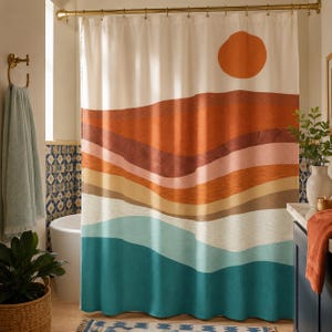 May include: A shower curtain featuring a landscape print with a large orange sun above layered horizontal bands of rust, terracotta, light pink, tan, cream, and teal colors. The curtain hangs from a gold rod with rings in a bathroom setting.