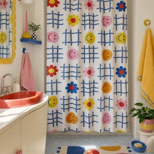 Könnte beinhalten: Ein weißer Duschvorhang mit einem sich wiederholenden blauen Gittermuster, durchsetzt mit bunten grafischen Symbolen wie gelben, rosa und orangefarbenen Smileys sowie roten, rosa und blauen Blumen, der an einer weißen Stange hängt.