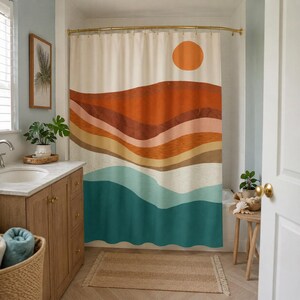 May include: A shower curtain featuring a landscape print with horizontal wavy bands of orange, terracotta, beige, and teal. A solid orange circle representing the sun is positioned in the upper right corner against a cream-colored background.