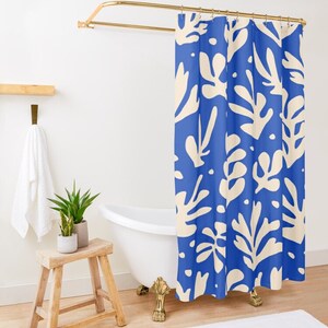 May include: A blue shower curtain with a cream leaf pattern hangs from a gold-coloured rod. The bathroom features a white bathtub with gold-coloured feet, a wooden stool, and a white towel.