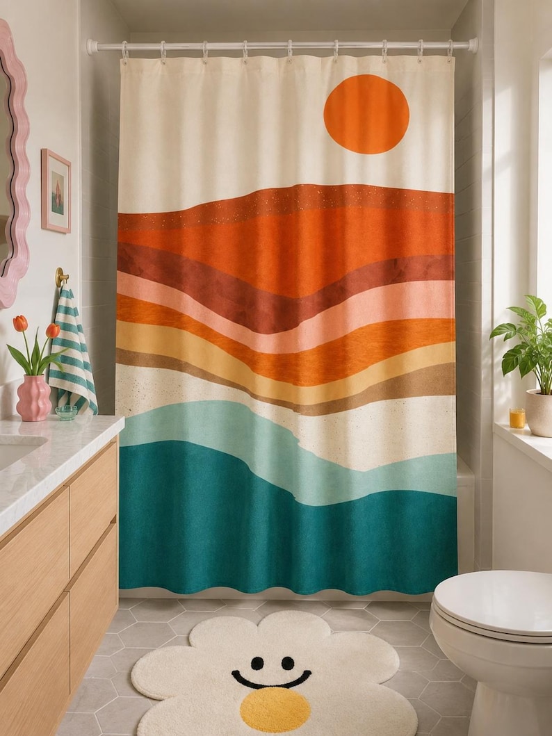 May include: A shower curtain featuring a landscape print with a large orange sun above layered horizontal bands of rust, terracotta, peach, tan, and teal colors. The curtain hangs from a white rod with rings and covers a bathtub area.