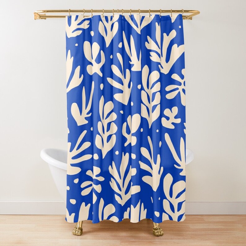 May include: A blue shower curtain featuring a repeating pattern of cream-coloured, leaf-like forms. The curtain hangs in front of a white bathtub with gold fixtures. The design is a modern, abstract botanical print.