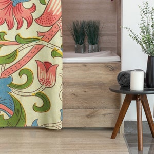 May include: A floral shower curtain with a cream background and a repeating pattern of pink, blue, and green flowers and vines. The curtain is partially open, revealing a white bath and a wooden floor.
