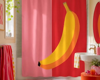 May include: A shower curtain featuring a split-color design with a solid light pink left side and a solid red right side. A large, stylized yellow banana graphic with an orange-toned shadow is centered across the red portion of the curtain.