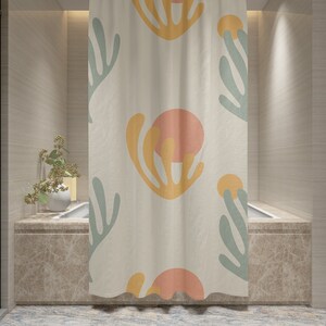 May include: A shower curtain with a white background and a repeating pattern of abstract shapes in shades of yellow, orange, and green.