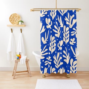 May include: A blue shower curtain featuring a repeating pattern of cream-coloured leaf shapes. The curtain hangs in front of a white bathtub with gold-coloured feet. A small wooden stool and a shelf with towels and decor are visible.